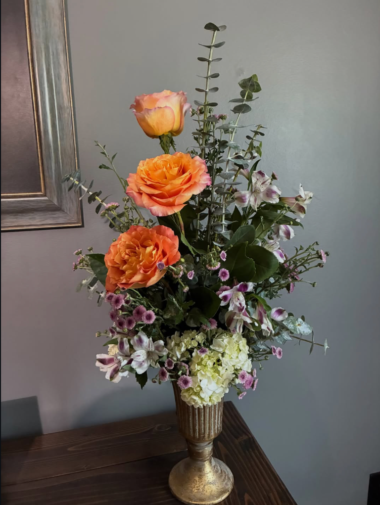 Orange roses and hydrangea arrangement in a gold vase
